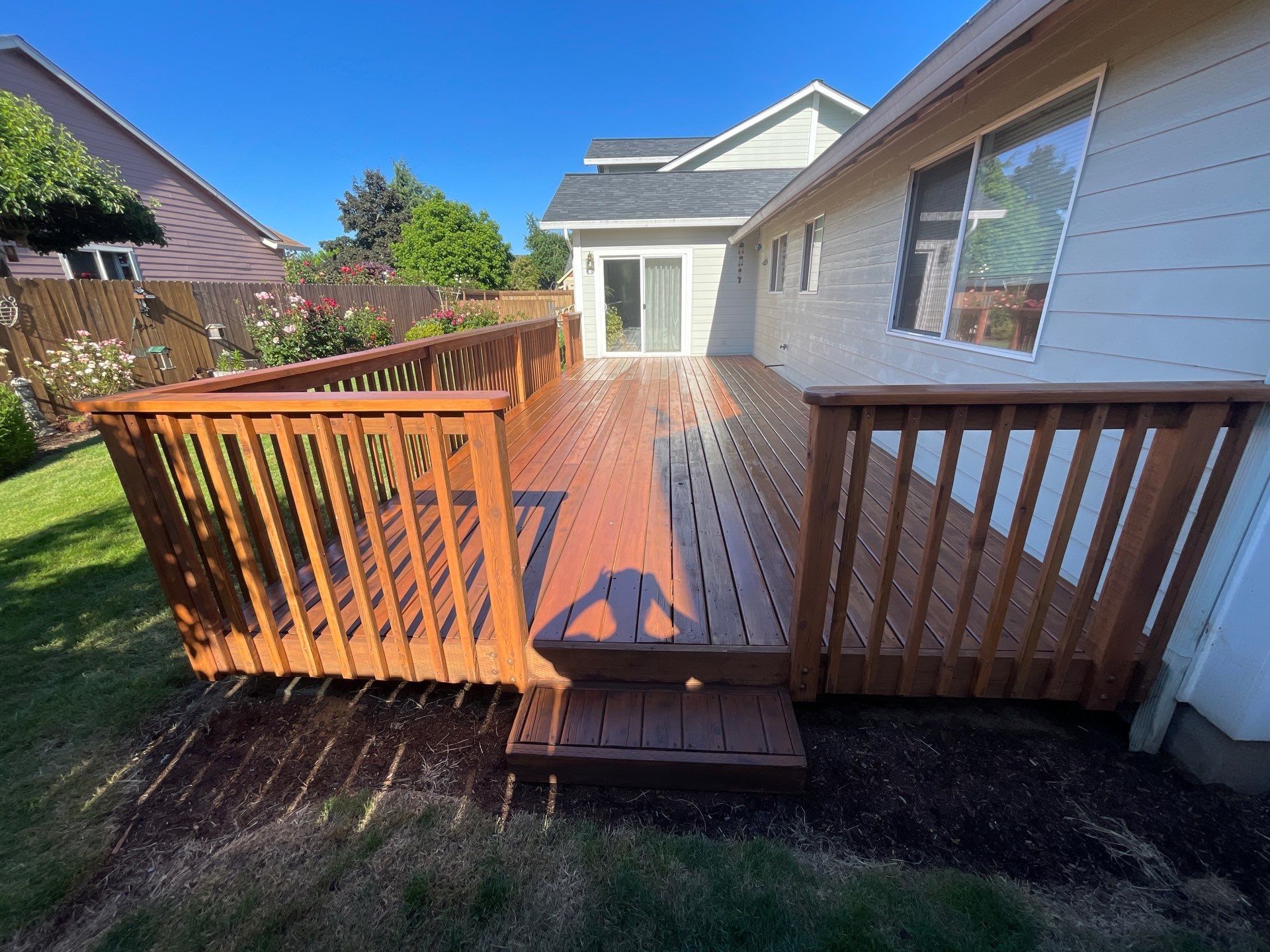 A wooden backyard deck with railings attached to a house, shown on a sunny day with shadows cast on the deck.